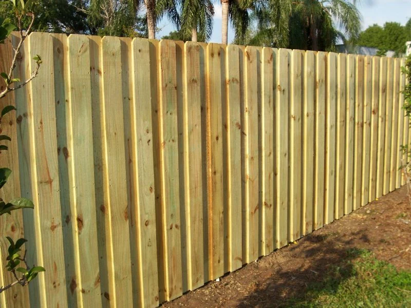 Board-on-board wood privacy fence with dog-ear pickets beside a landscaped yard